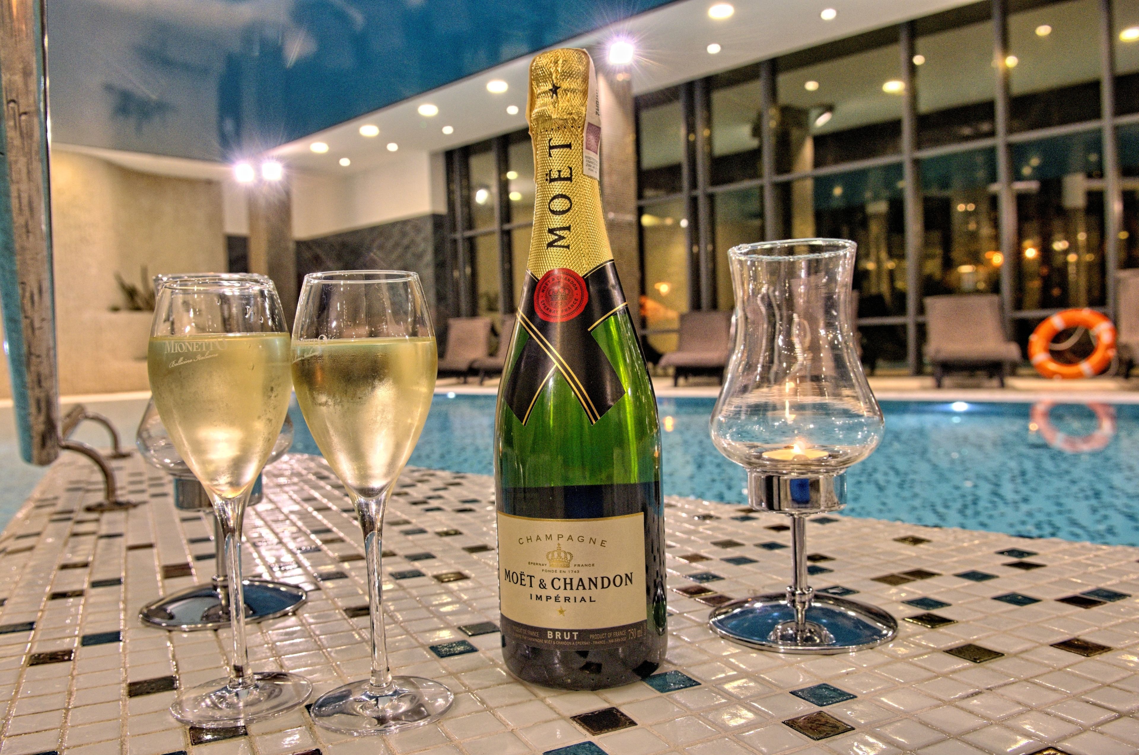 A bottle of Moët & Chandon champagne, two filled glasses, and one empty glass on a tiled poolside table.