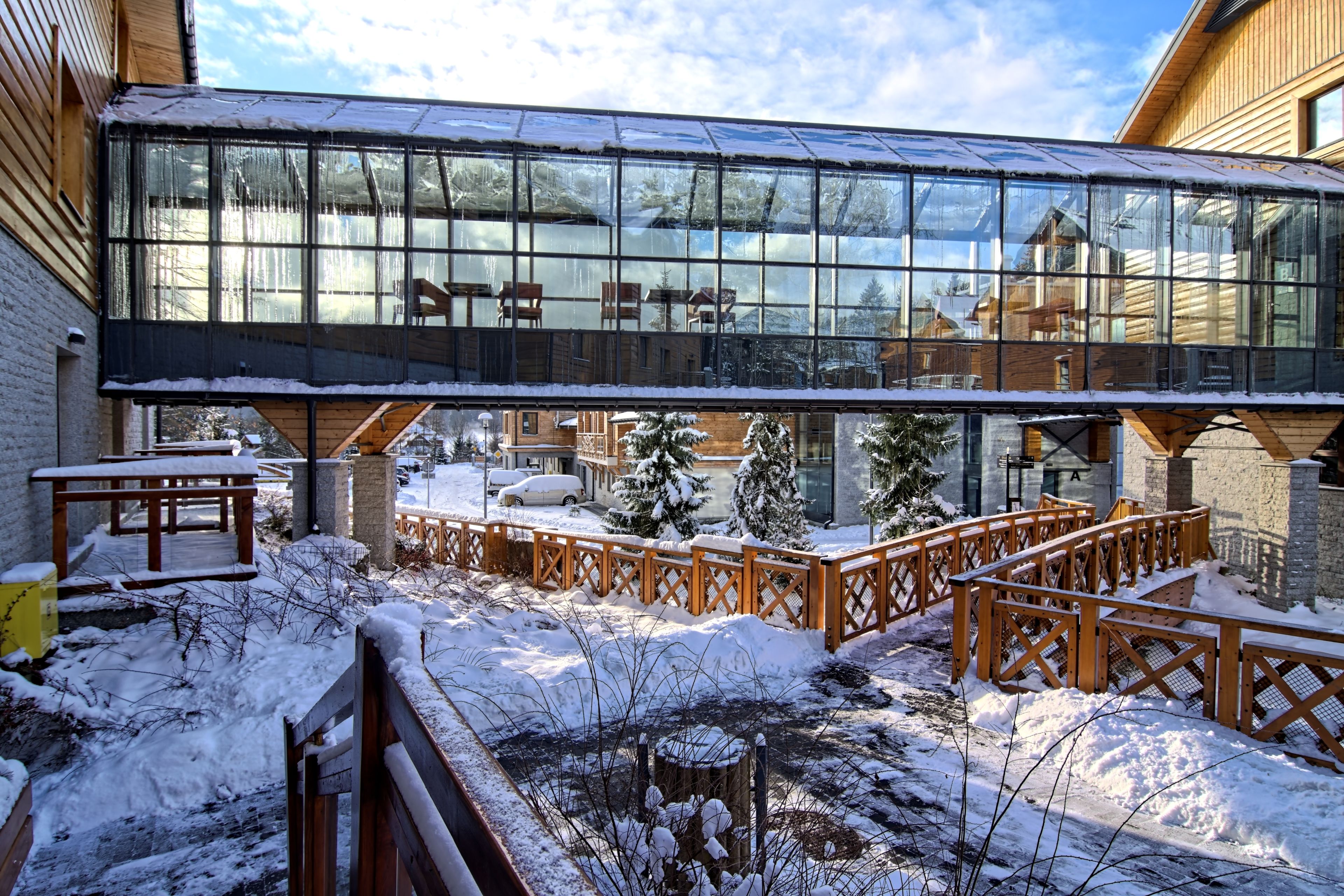 A modern building with large glass windows, wooden deck, and snow-covered surroundings.