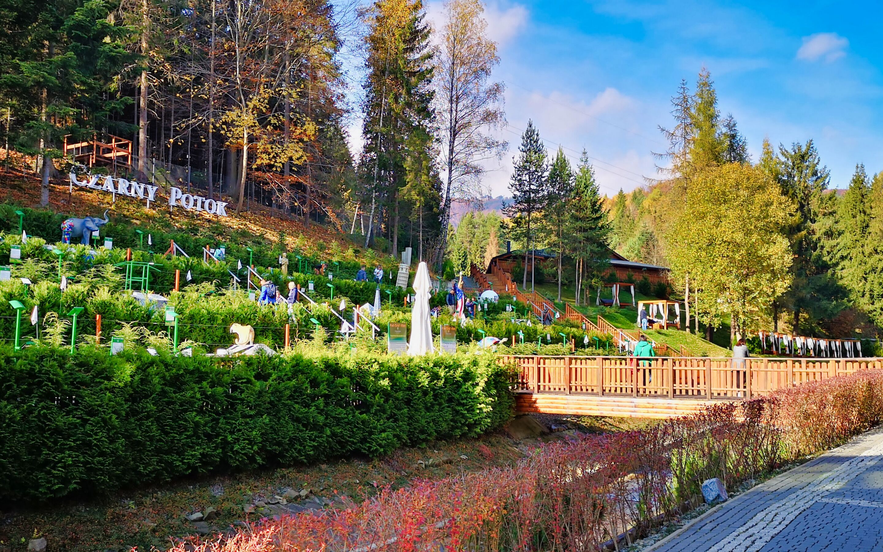 A park with a wooden bridge, a statue, and a sign reading "LEARNY POTOK".
