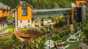 Un resort con edificios de madera, un pasillo de cristal y un paisaje verde exuberante.