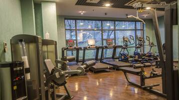 A gym with various exercise equipment, large windows, and a wooden floor.