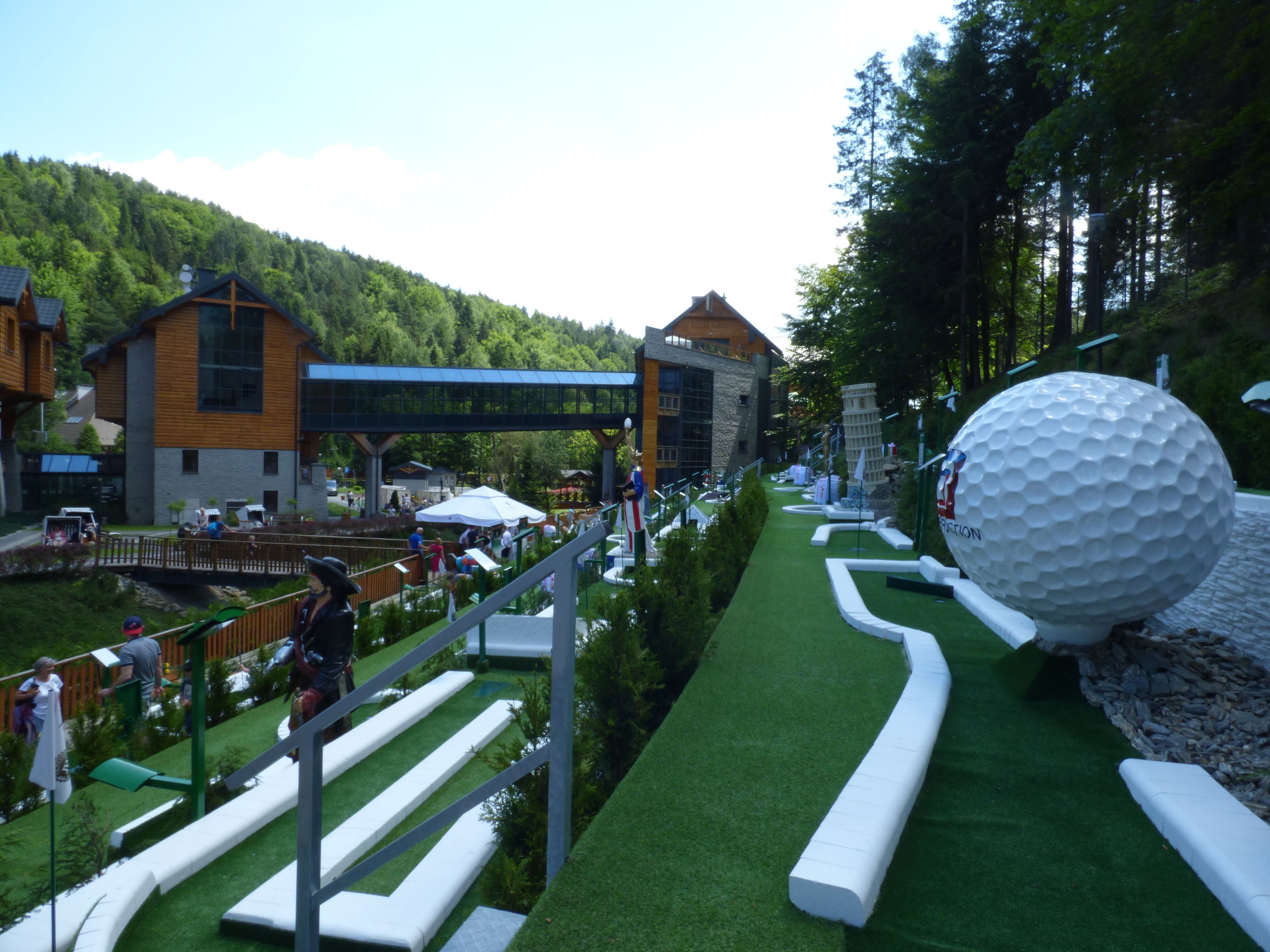 A golf course with a large golf ball sculpture, a bridge, and buildings in the background.
