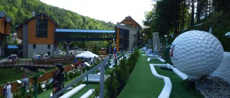 A golf course with a large golf ball sculpture, a bridge, and buildings in the background.