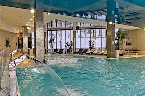 An indoor swimming pool with a clear water feature, lounge chairs, and large windows with a view of trees. - Hotel Czarny Potok Resort SPA & Conference (Krynica-Zdroj)