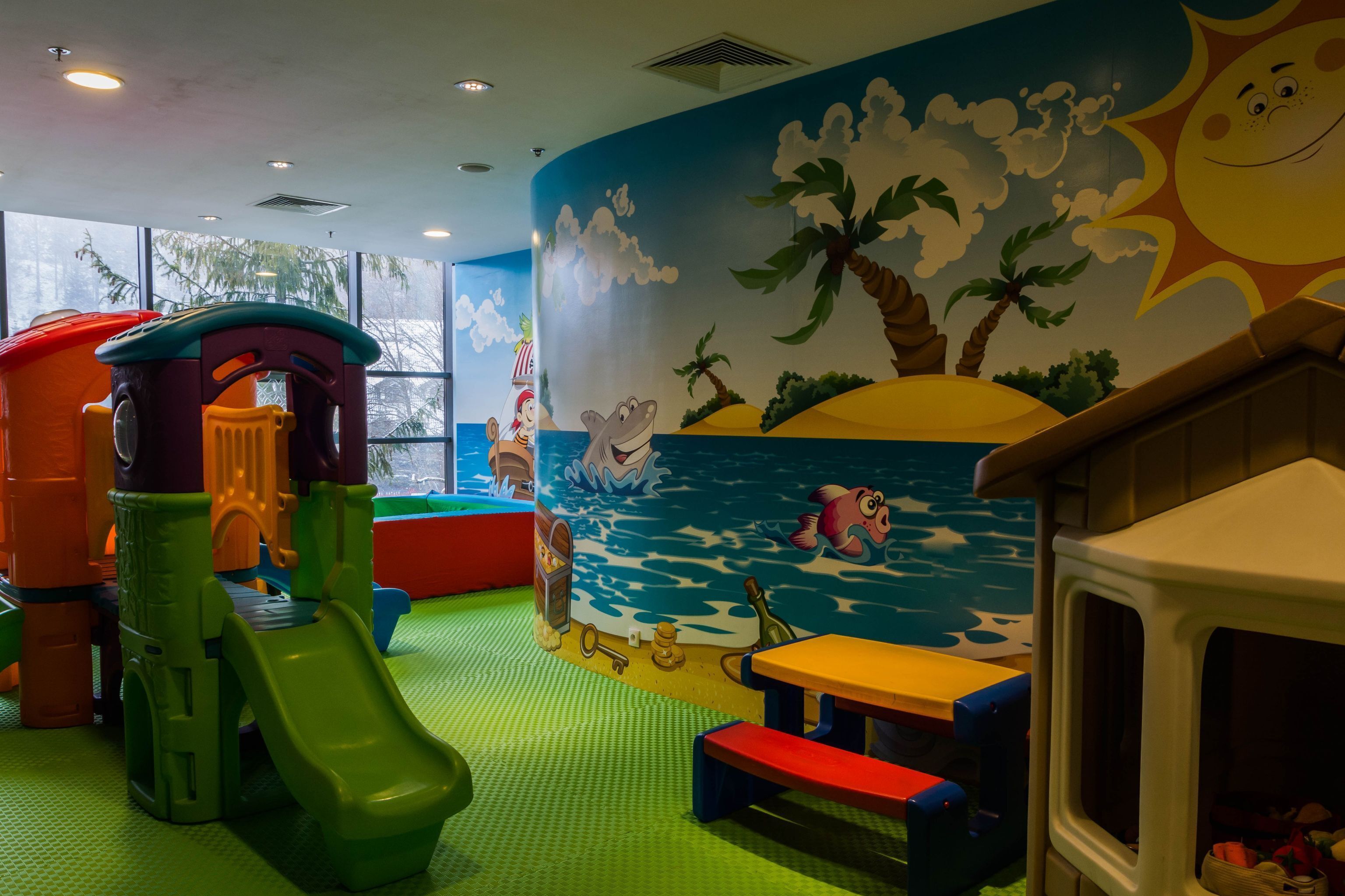 Ein Kinderspielbereich mit Rutsche, Spielgeräten und einer Wandmalerei mit Strandmotiv.