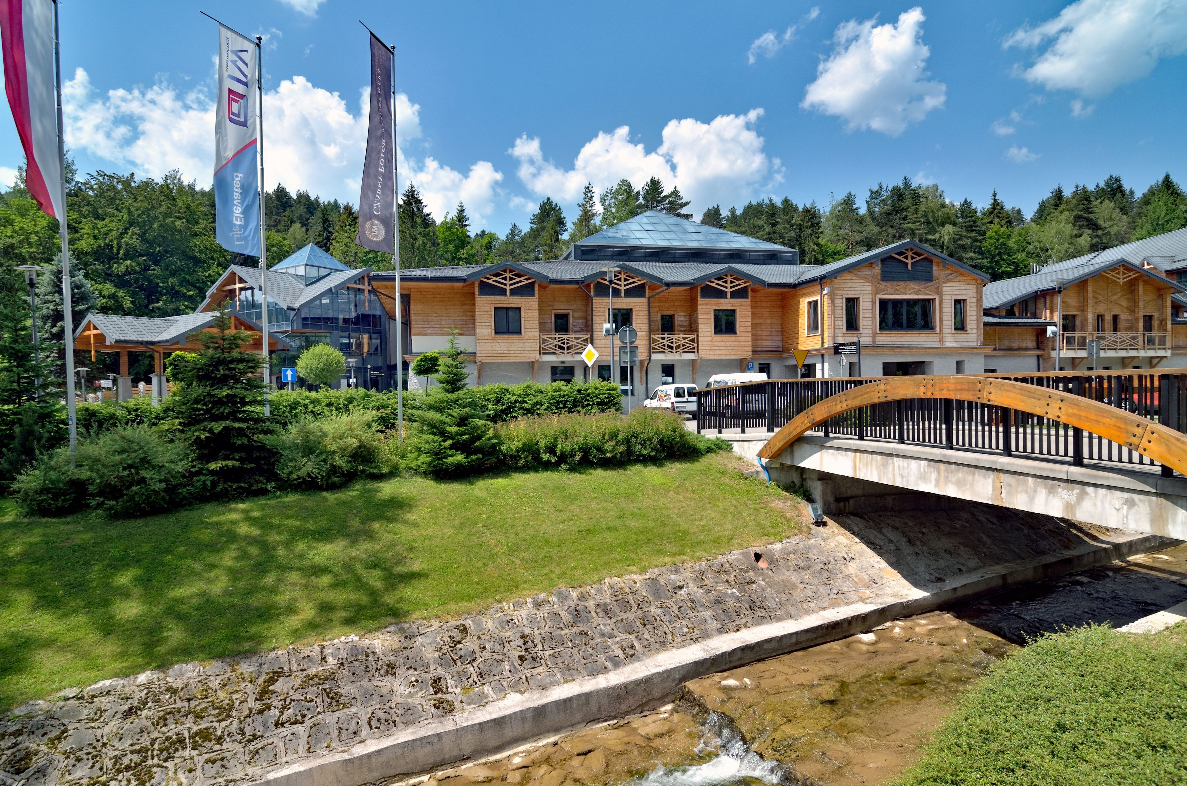 A hotel with multiple wooden cabins, a stone bridge, and a grassy area with flags.