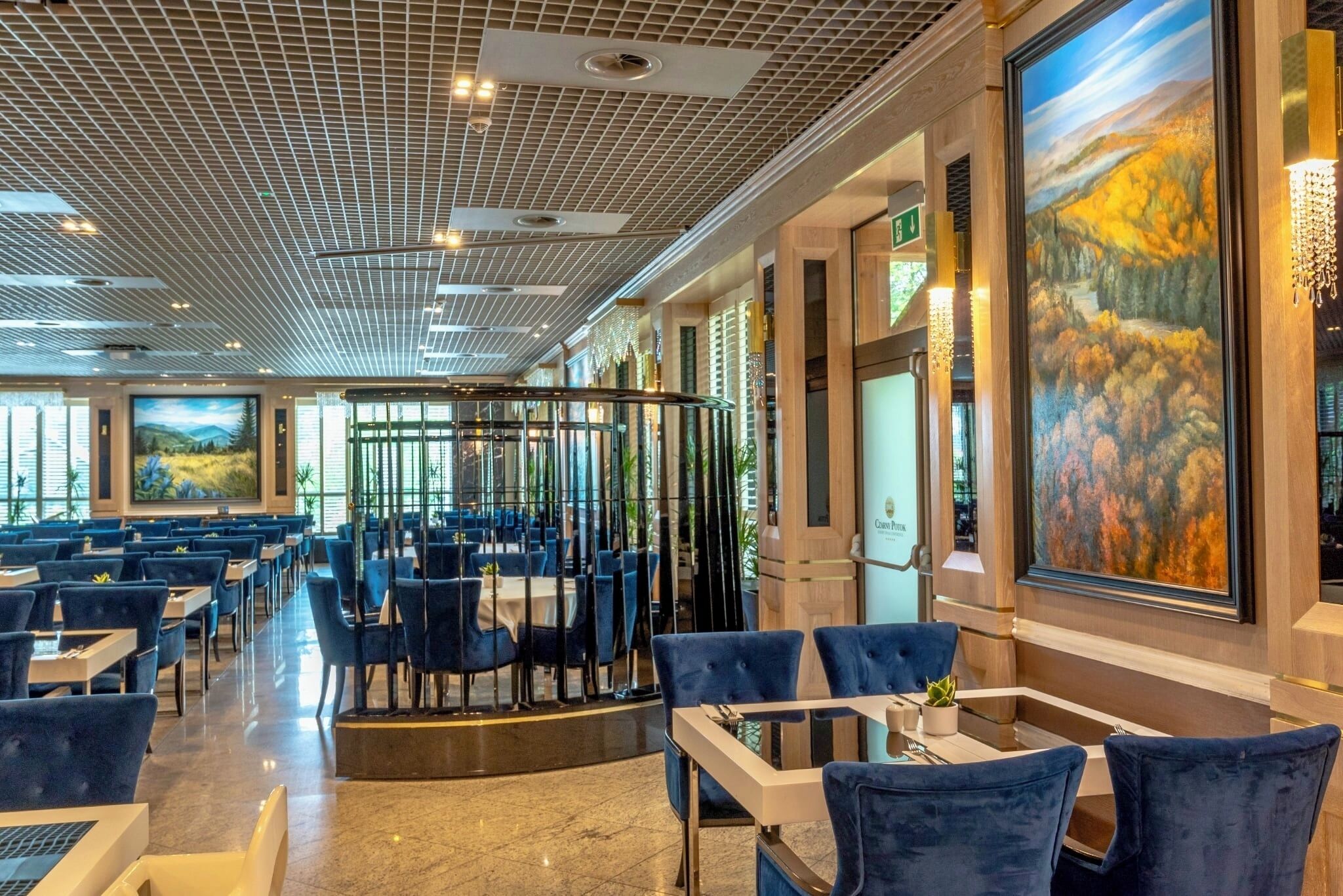 Een ruim restaurant met hoge plafonds, modern licht en grote ramen met uitzicht op de omgeving.