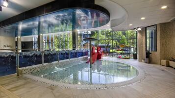 A modern indoor pool area with a glass enclosure, large windows, and a central red structure.
