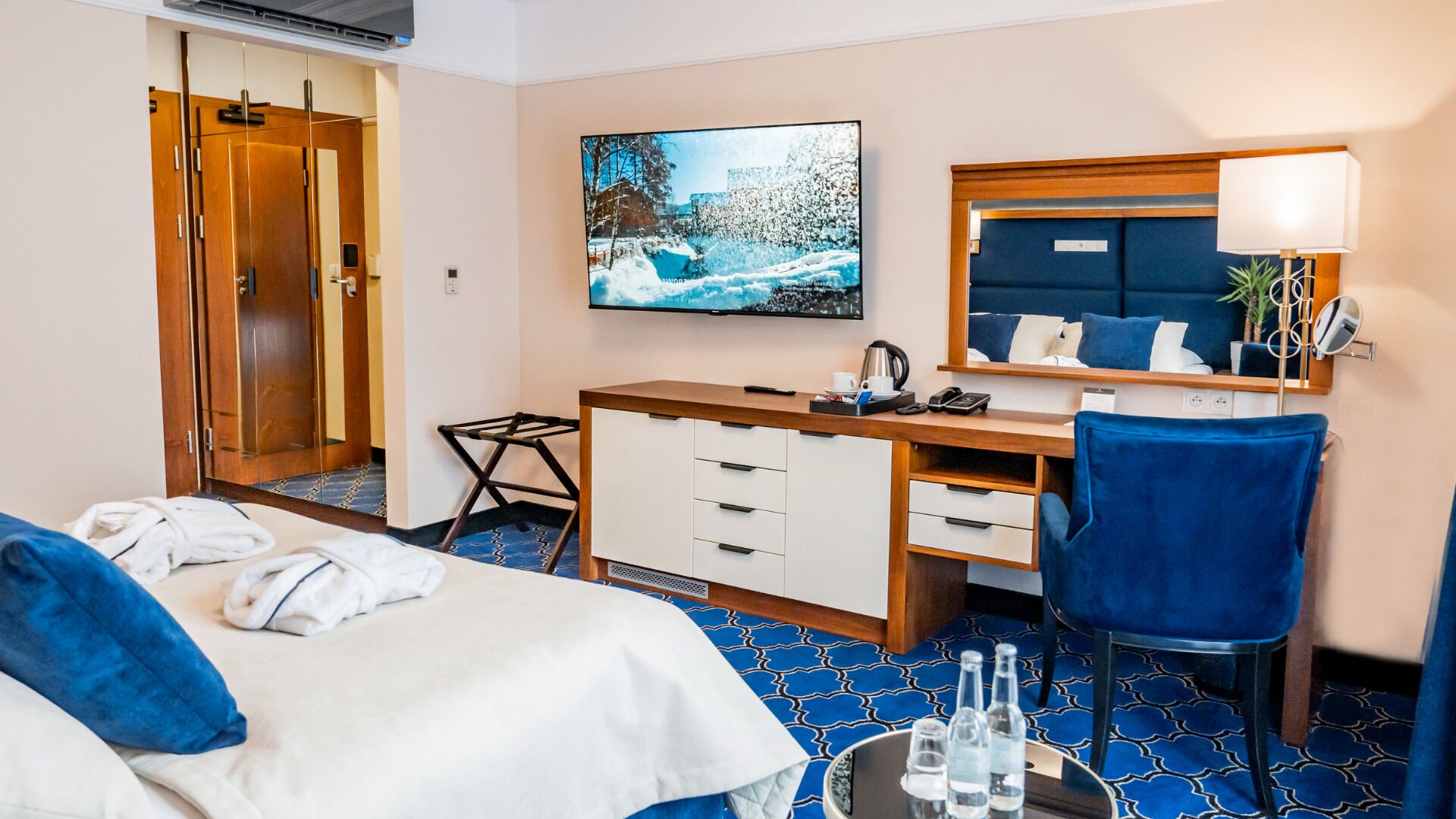 Une chambre d’hôtel avec un lit, un bureau, une chaise, un miroir, une télévision et une fenêtre donnant sur un paysage enneigé.