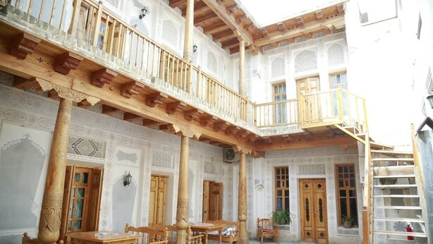 Un patio con mobiliario de madera, columnas y puertas decoradas.
