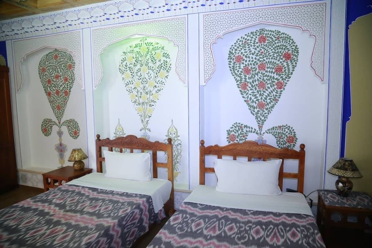 Una habitación con dos camas de madera, cada una con un cojín blanco y una colcha estampada. Las paredes presentan diseños florales detallados.