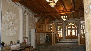A spacious interior with a wooden staircase, a seating area with chairs, and a decorative wall with geometric patterns. - Komil Bukhara Boutique Hotel (Bukhara)