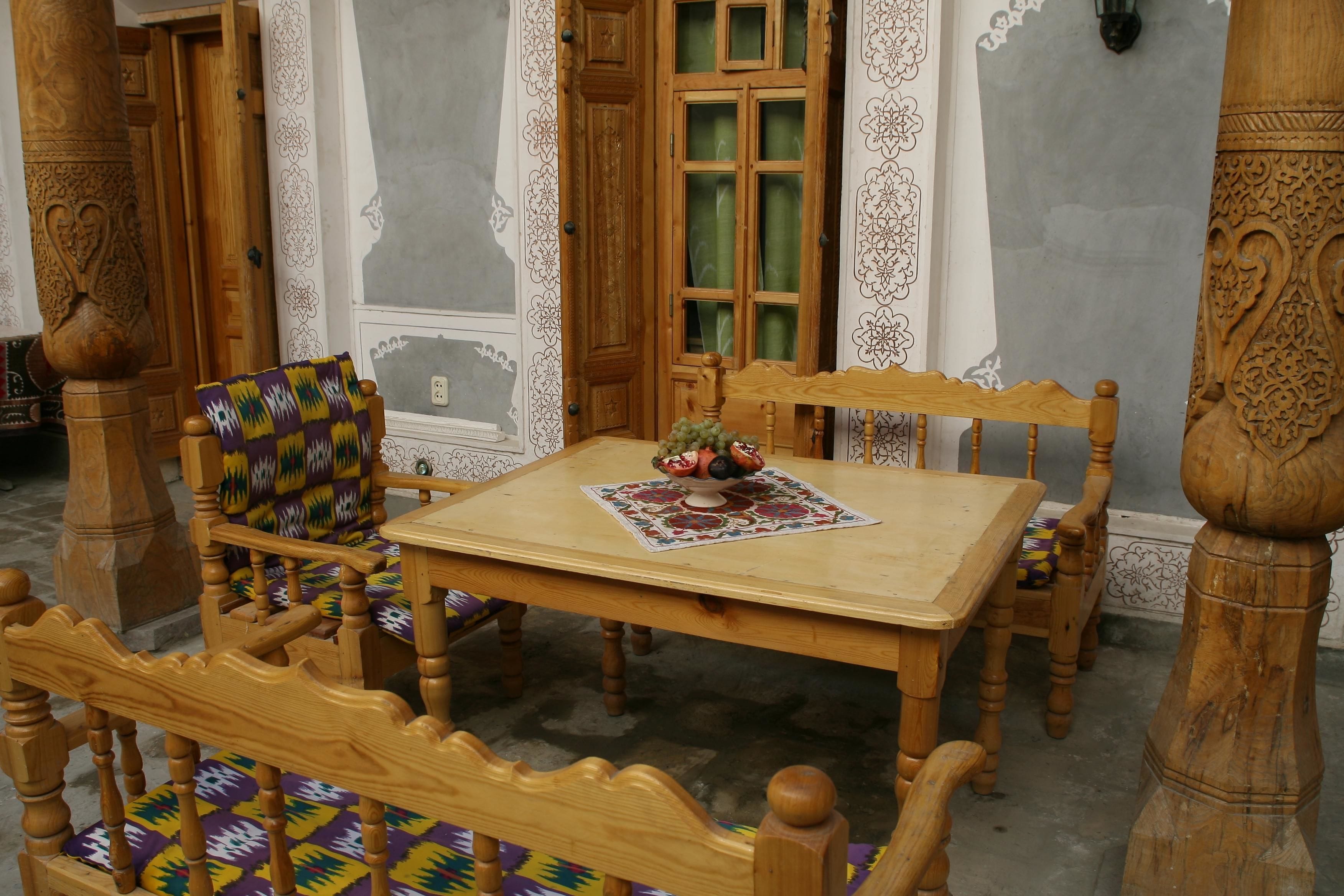 Una mesa de comedor de madera con un camino de mesa estampado, rodeada de sillas de madera con cojines de colores.