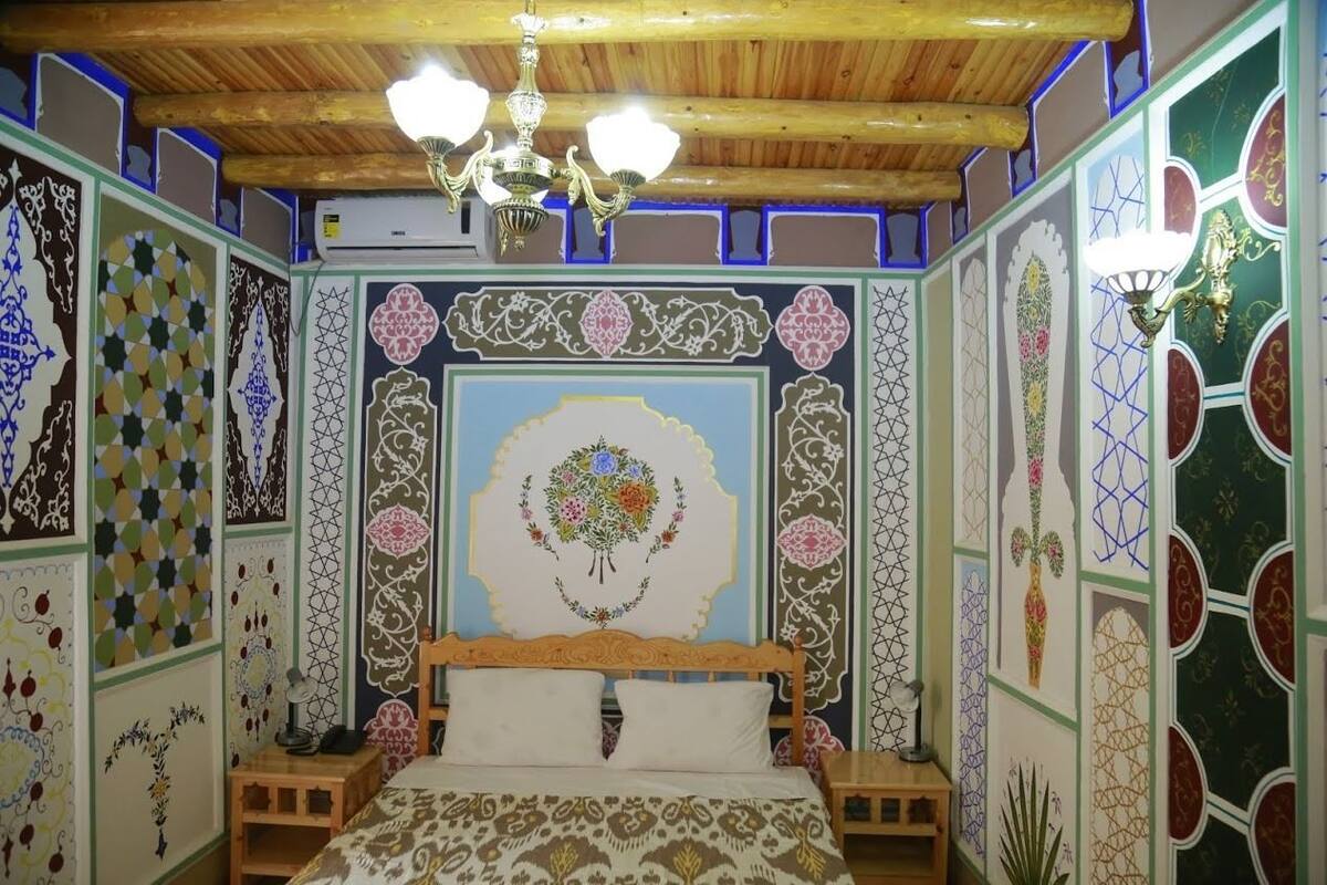 Una habitación tradicional con techo de madera, decoraciones ornamentales en la pared, una cama con colcha estampada y un candelabro.