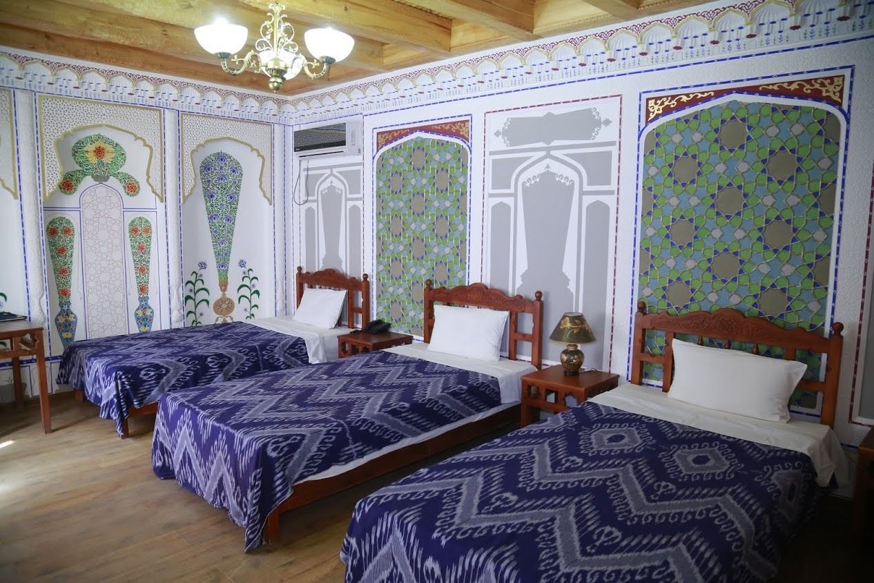 A traditional room with three beds, wooden headboards, and patterned wall decorations.