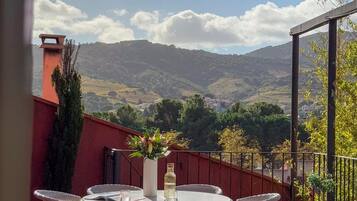 Une terrasse dotée de chaises et d’une table en osier, offrant une vue sur un paysage montagneux.