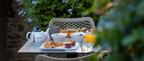 A breakfast table with a croissant, cereal, juice, and a coffee pot.