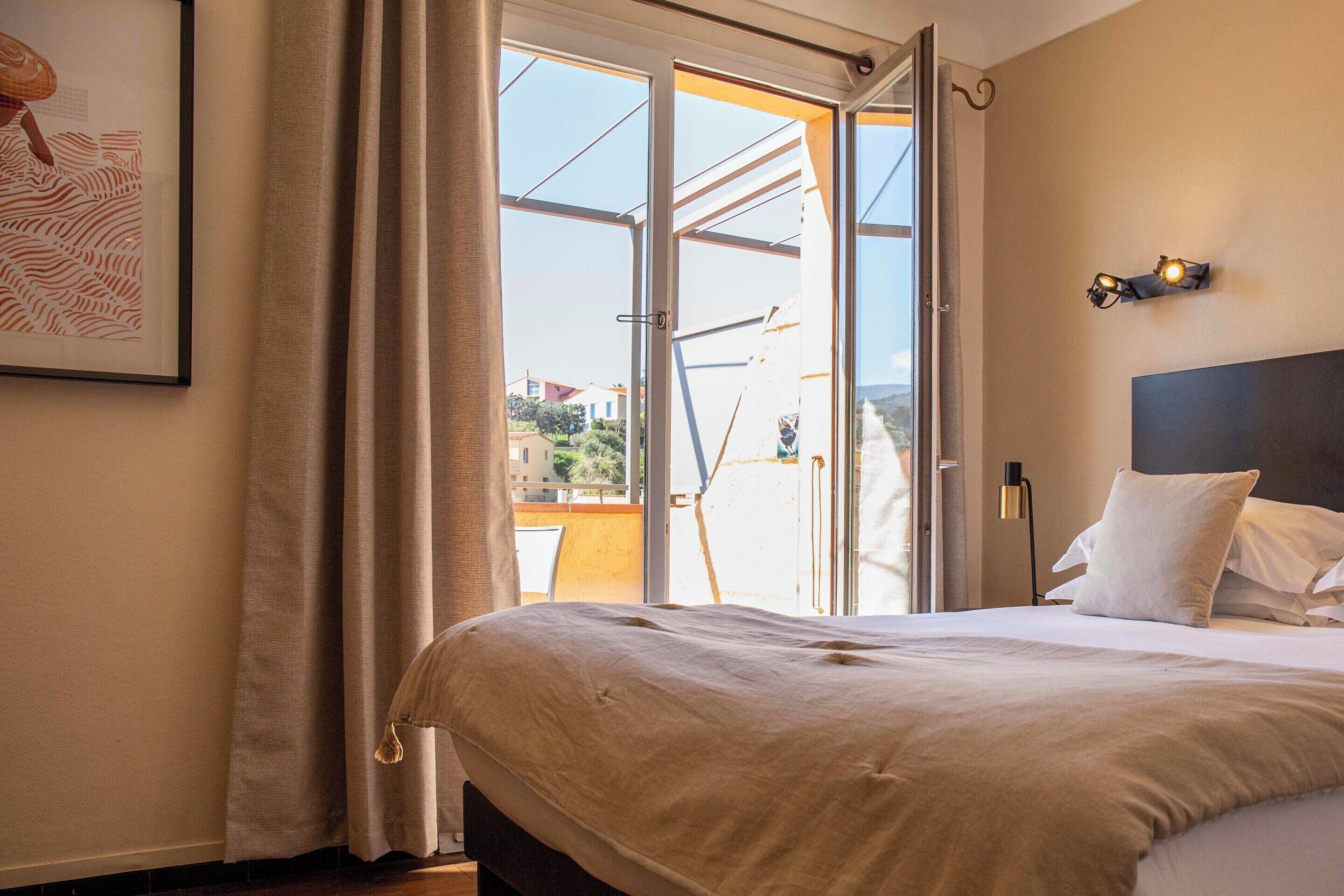 A bedroom with a bed, a large window, and a view of the outside.