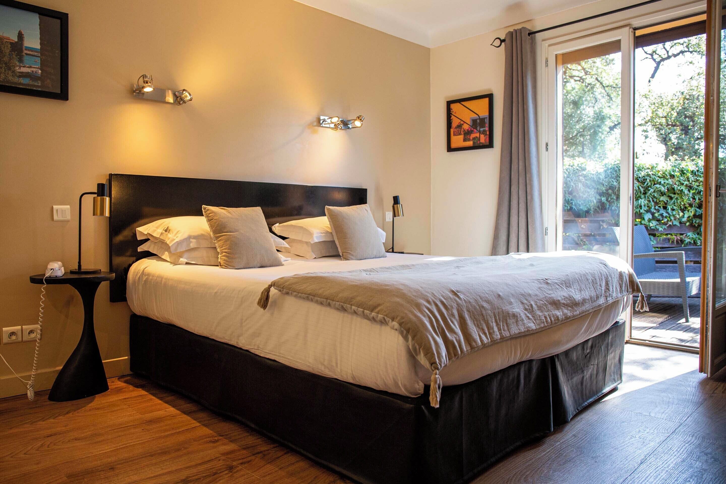 Habitación de hotel con una cama grande, mesitas de noche y vistas a través de un ventanal corredero.