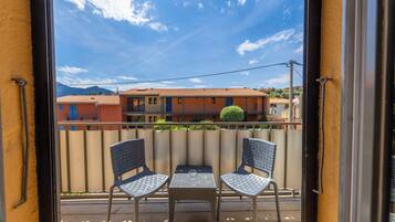 A balcony with two chairs and a table, overlooking a row of buildings and a mountain.