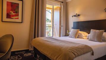 Een hotelkamer met een bed, een stoel, een lijst met foto en een balkon met gordijnen.