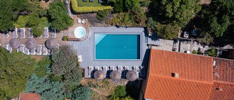 Vista aérea de una propiedad con piscina, sillas de descanso y jardín.