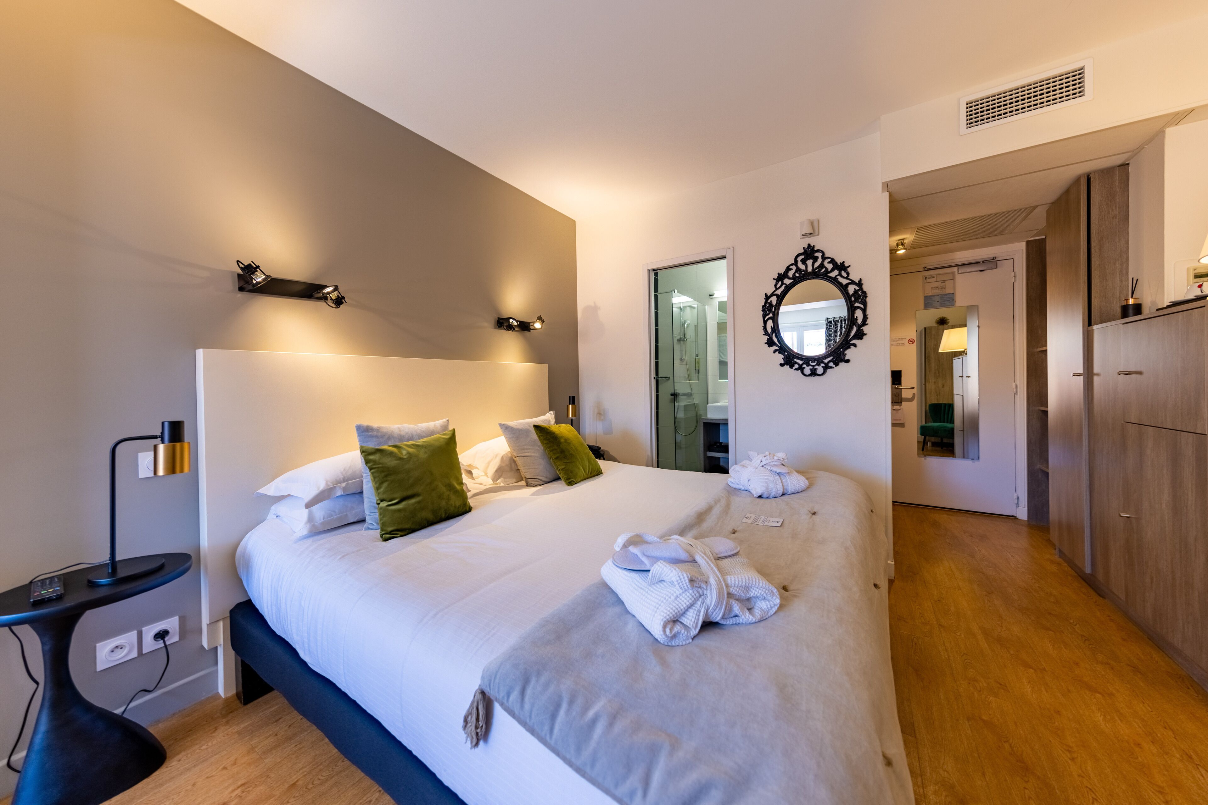 A modern hotel room with a large bed, bedside tables, a mirror, and a wardrobe.