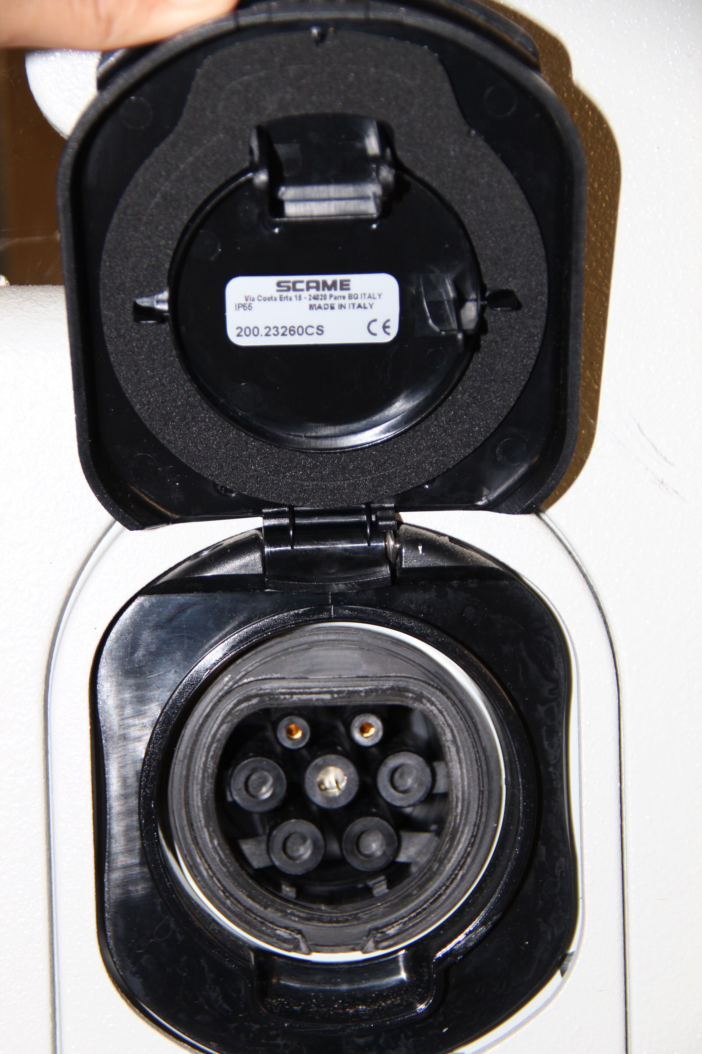 An open electrical plug with a label indicating it is a SCAMEG device, made in Italy, and has a CE mark.
