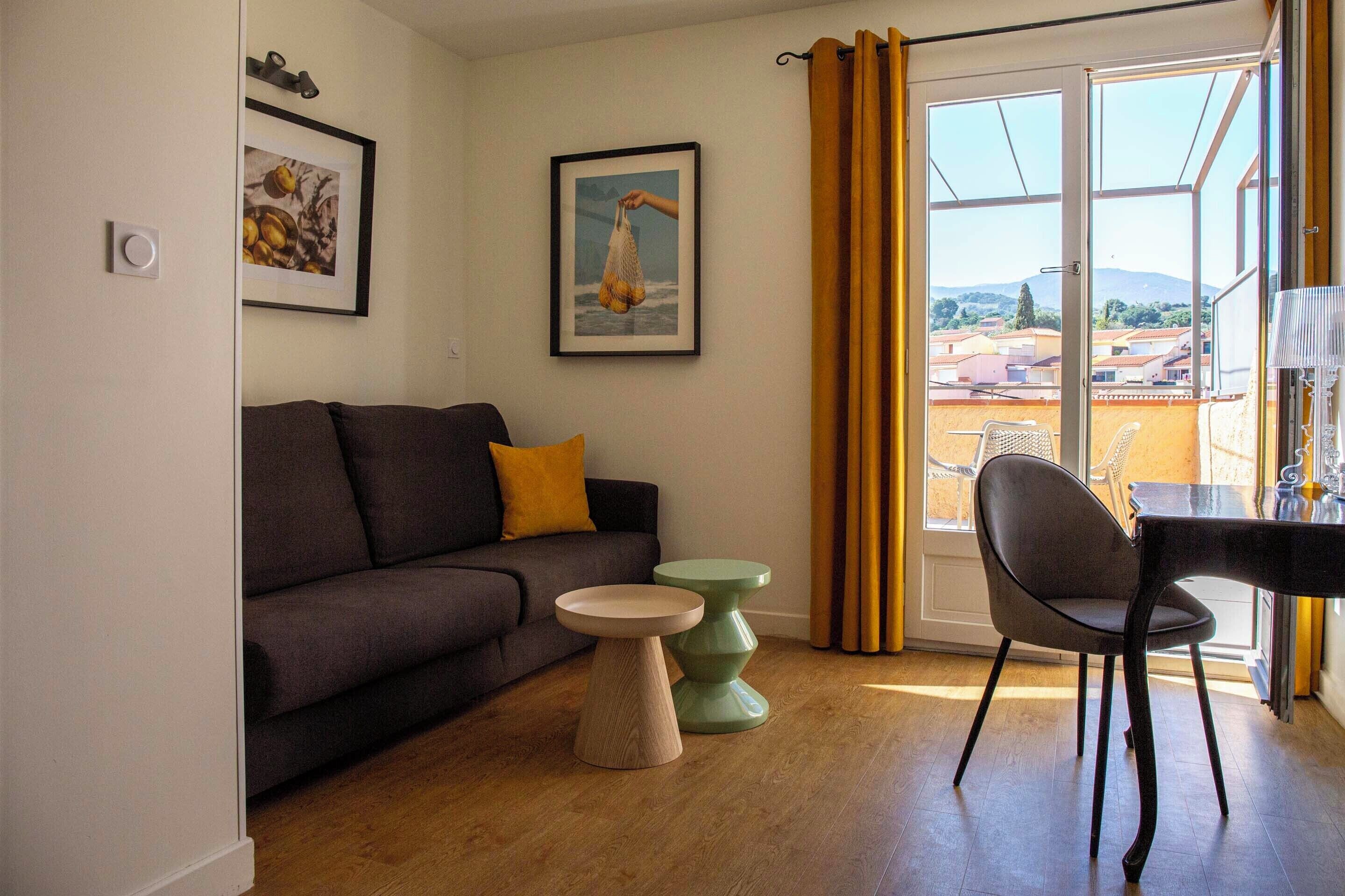 Una sala de estar con sofá, dos mesitas auxiliares, una silla y un balcón con vistas.