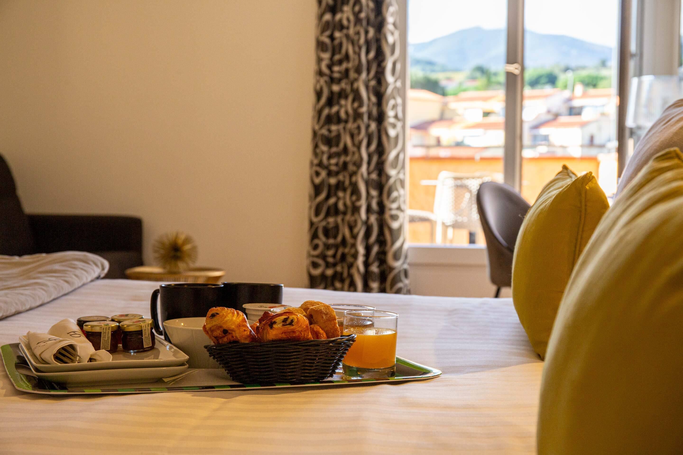 A neatly made breakfast tray with pastries, a cup, and a glass of orange juice on a bed with a view of the outdoors.
