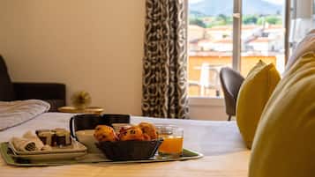 A neatly made breakfast tray with pastries, a cup, and a glass of orange juice on a bed with a view of the outdoors.