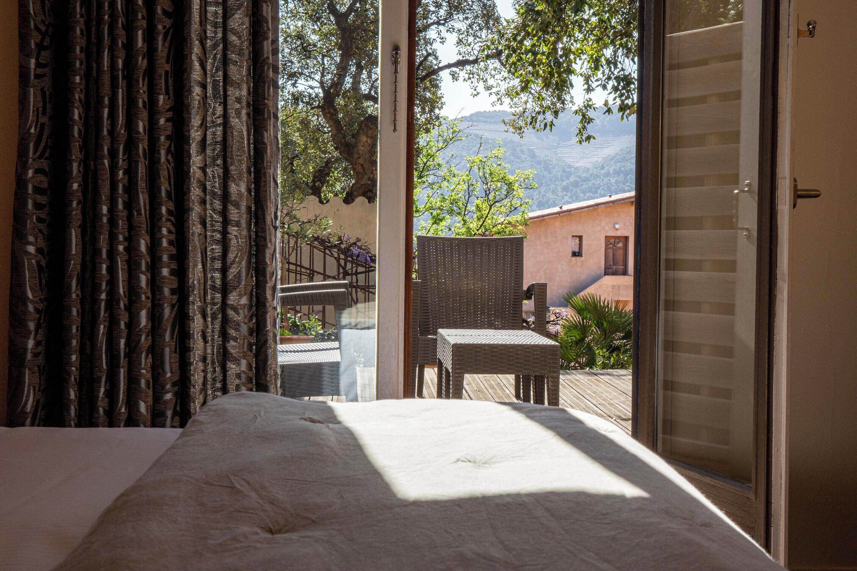 Un dormitorio con una cama grande, un ventanal corredizo que da a un balcón con mobiliario exterior y vistas a la montaña.