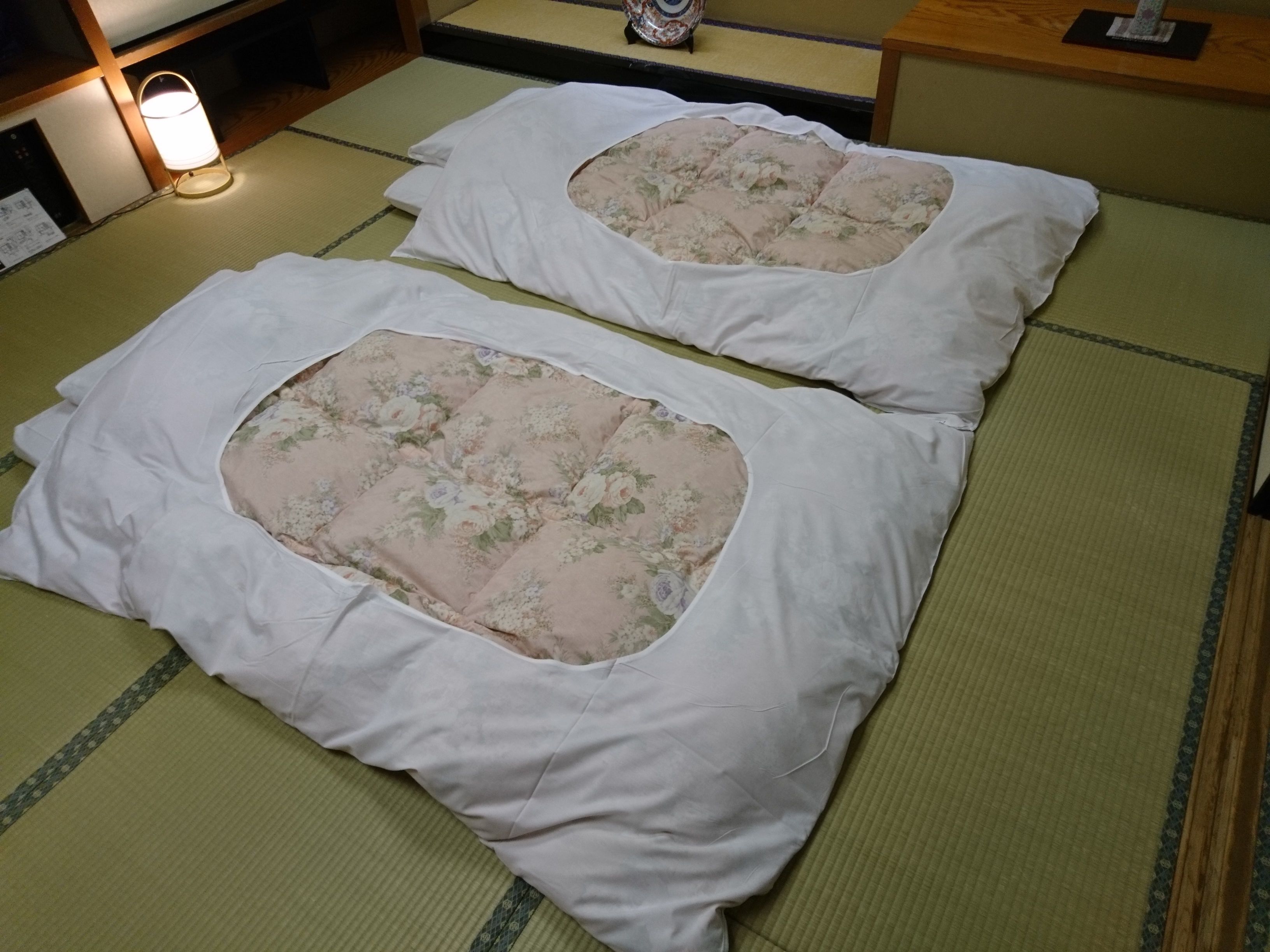 Two tatami mat beds with white bedding and floral-patterned cushions.