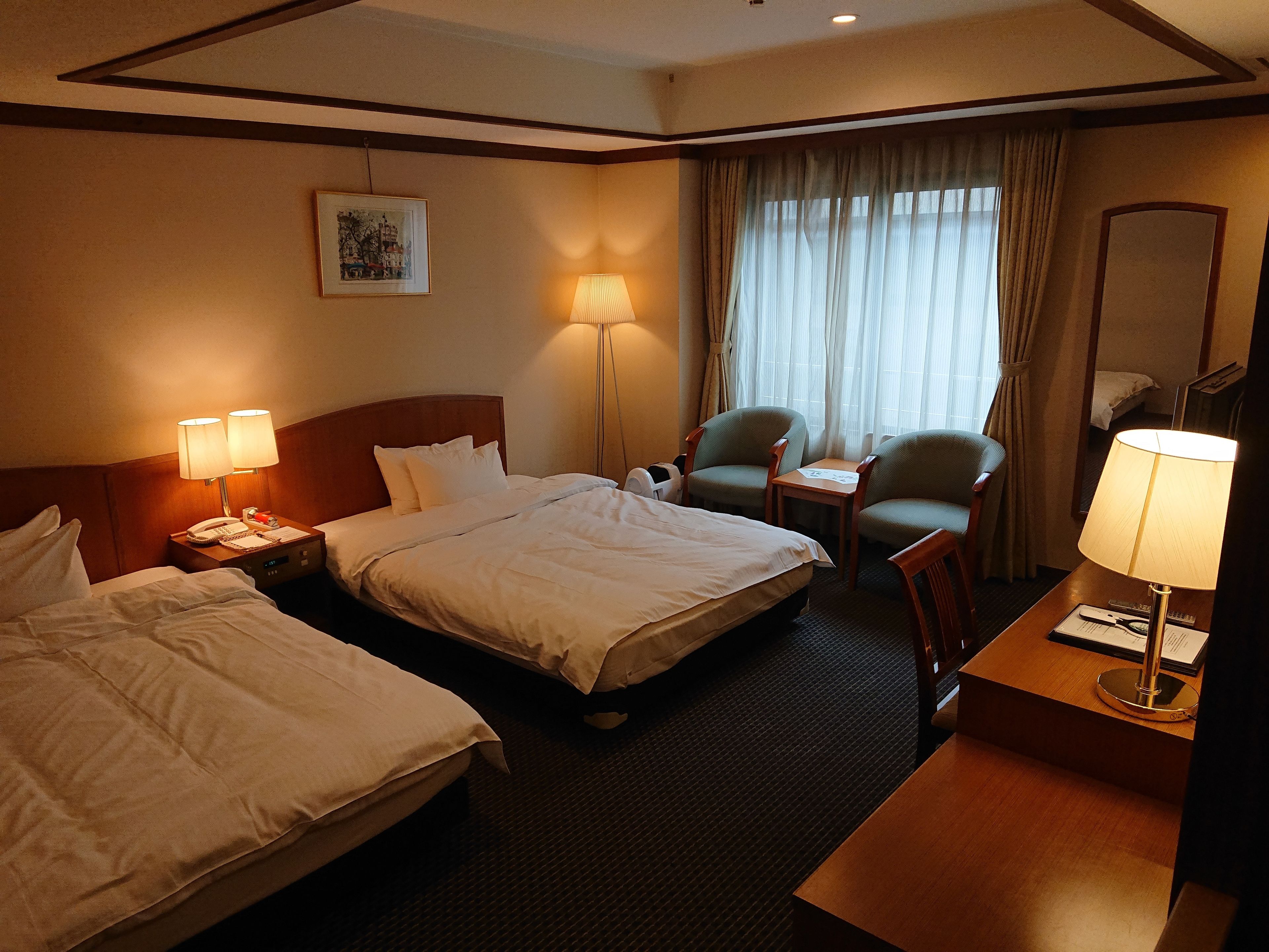 Habitación de hotel con dos camas, un escritorio, una silla, una lámpara y un cuadro en la pared.