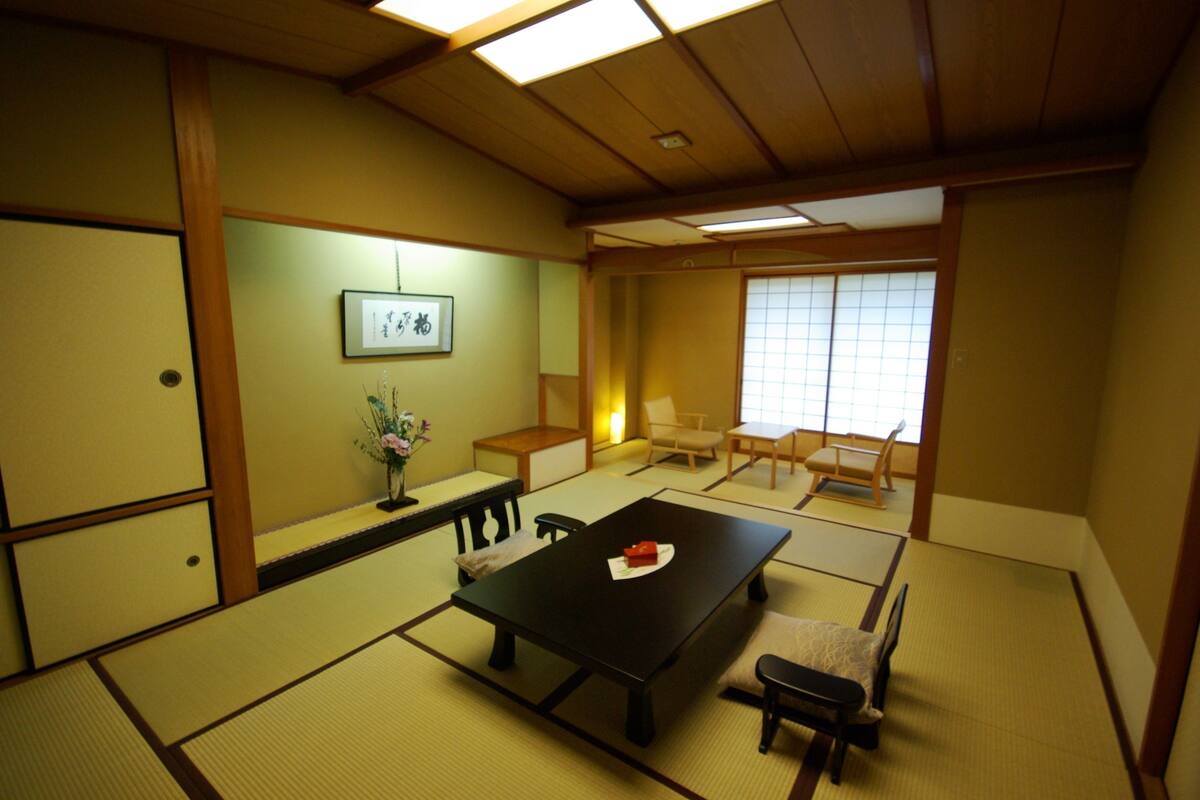 A traditional Japanese room with tatami flooring, a low table with a red object, and sliding doors.