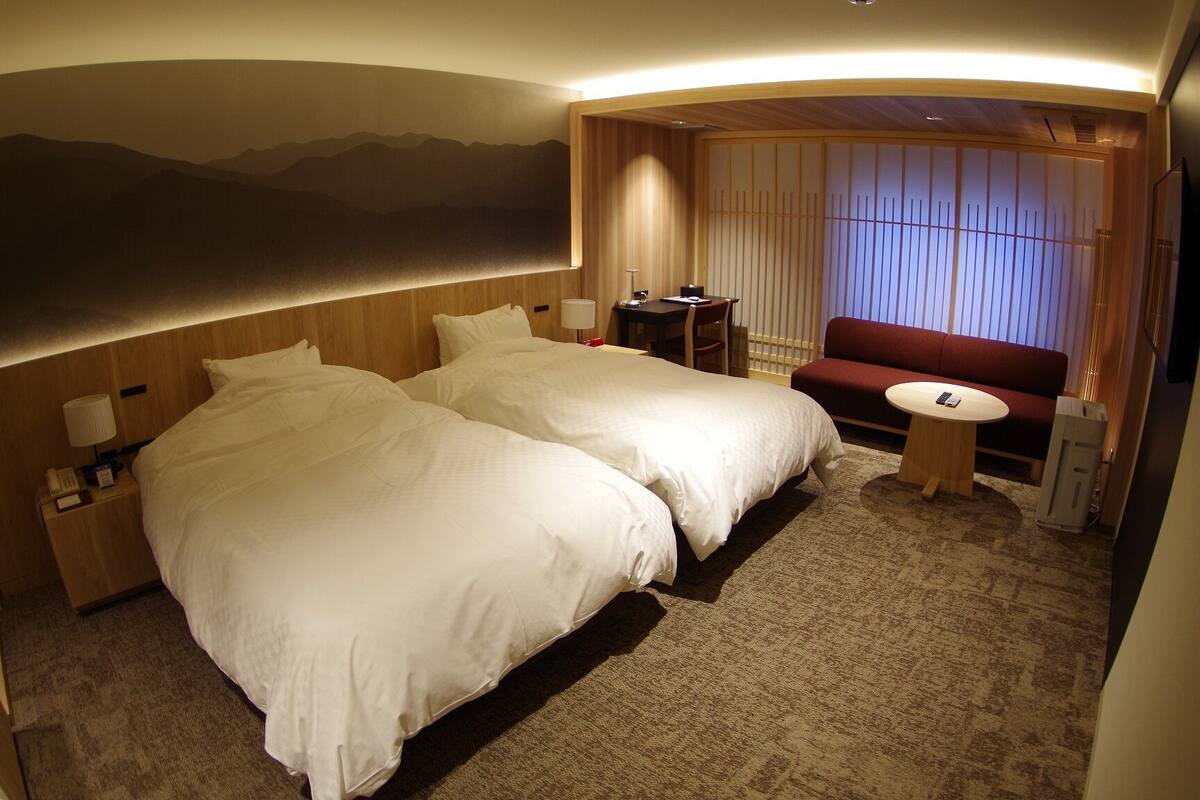 A hotel room with two beds, a small table, a sofa, and a view of mountains.