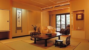 Et traditionelt japansk rum med tatamimåtter, et lavt bord, stole, en massagestol og et stort vindue.