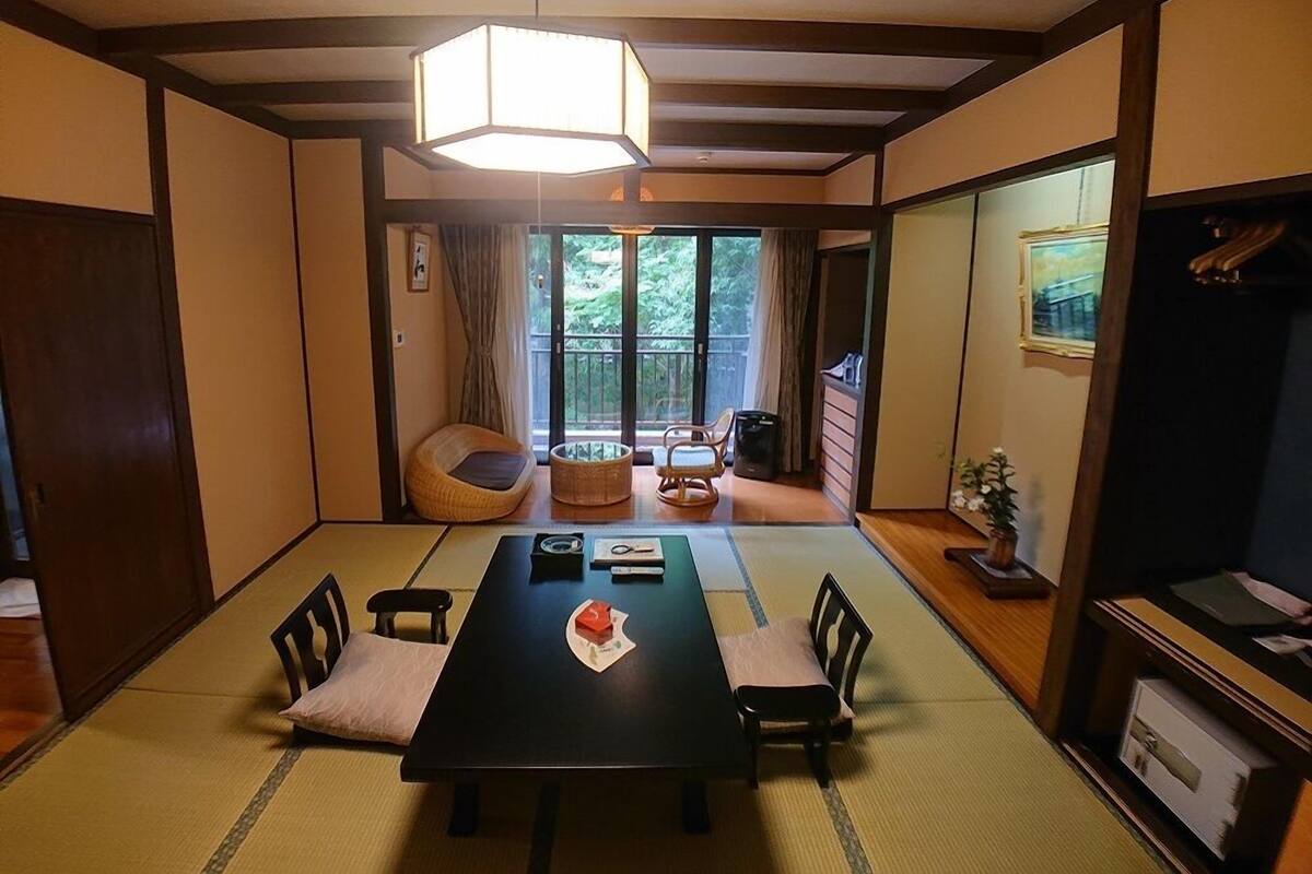 A traditional Japanese room with tatami flooring, a low table with cushions, and a sliding door leading to a balcony.