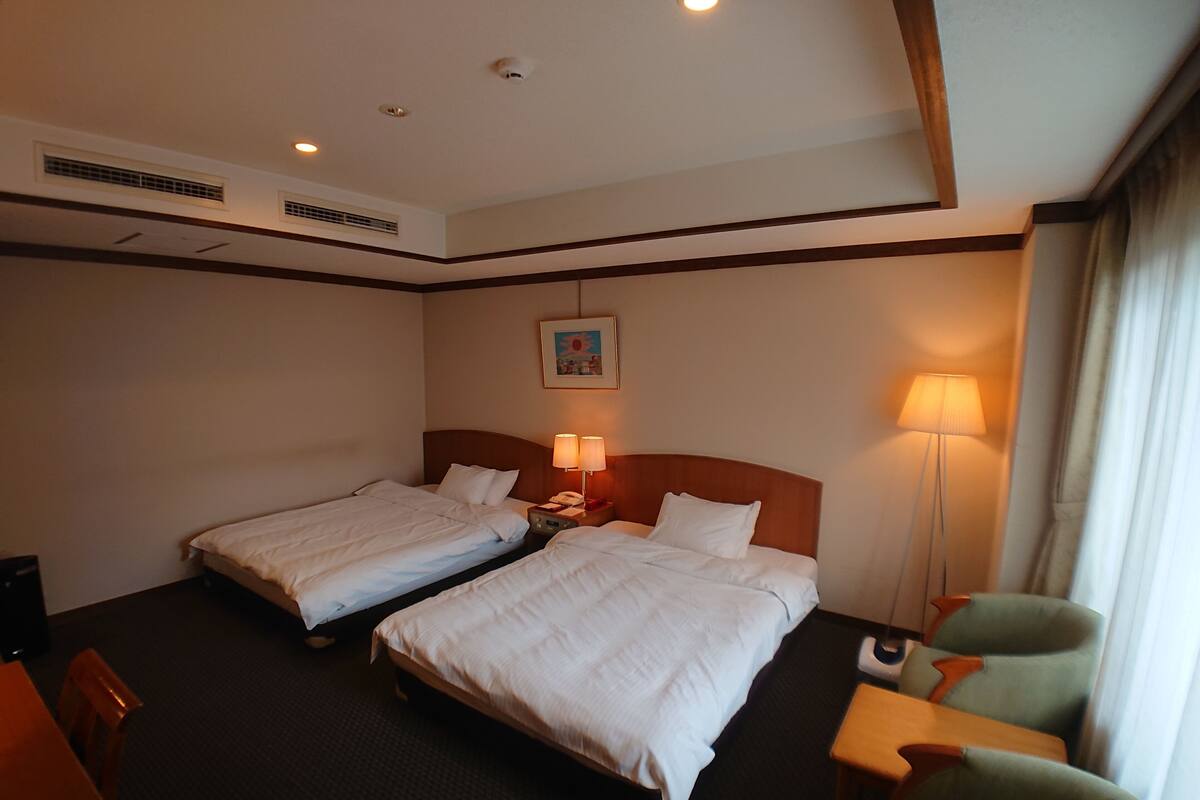 A hotel room with two beds, a desk, a chair, a lamp, and a painting on the wall.