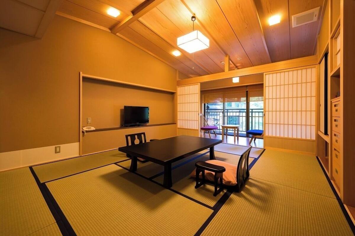 A traditional Japanese room with tatami flooring, a low table, chairs, a television, and sliding doors.