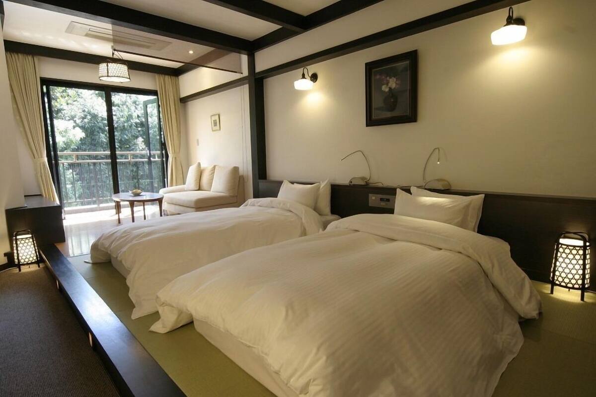 A hotel room with two beds, a desk, a chair, and a large window.