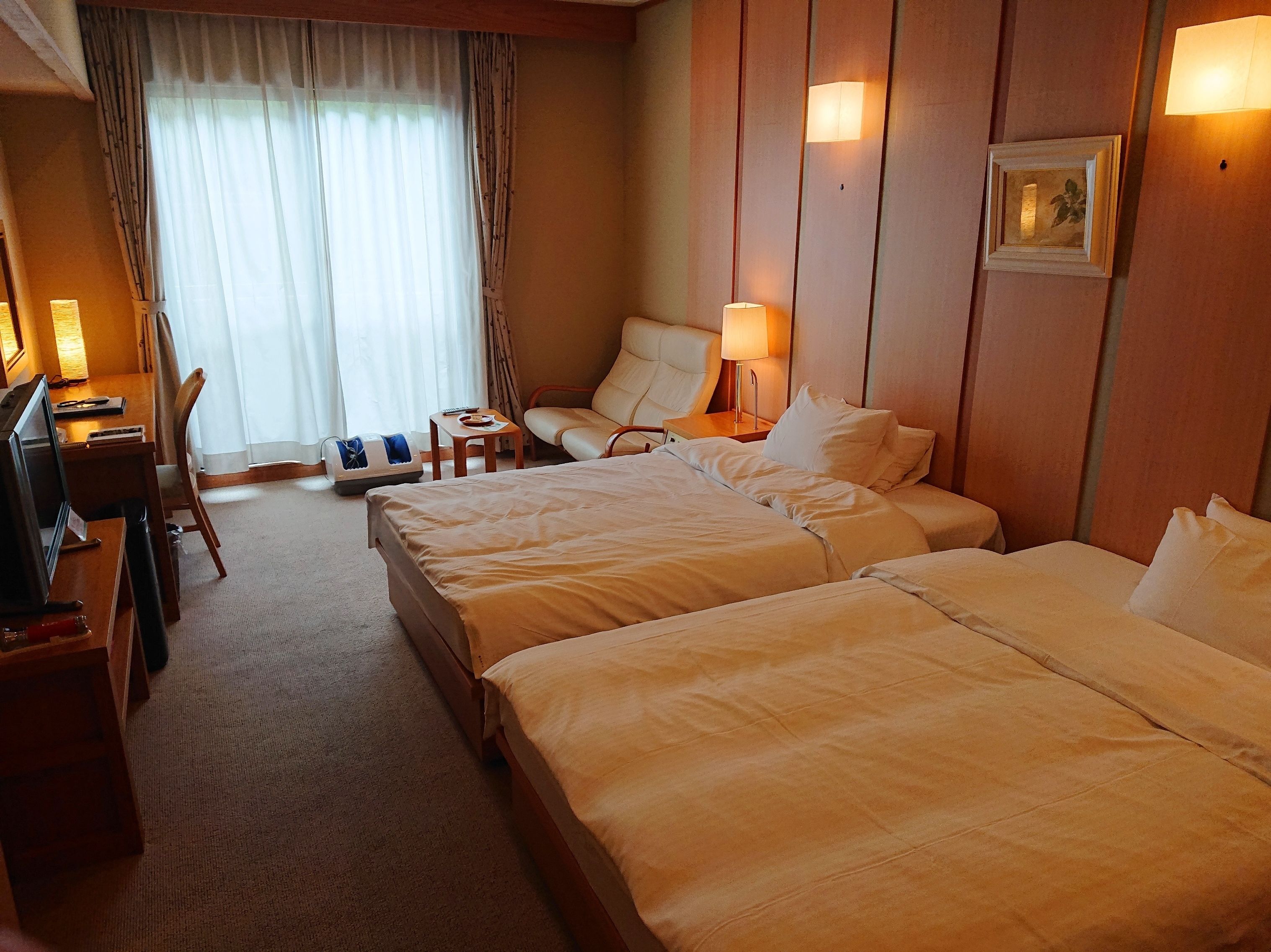 A hotel room with two beds, a desk, a chair, a lamp, and a picture on the wall.