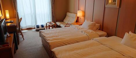 A hotel room with two beds, a desk, a chair, a lamp, and a picture on the wall.