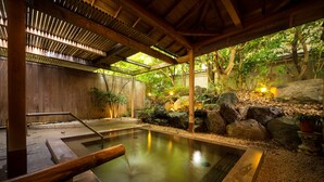 En traditionel japansk onsen med en træterrasse, en stenkilde og en naturlig stenvæg.