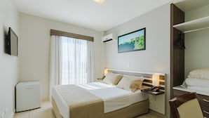 Une chambre d’hôtel avec un lit, une table de chevet avec une lampe, un téléviseur fixé au mur et une fenêtre avec des rideaux.