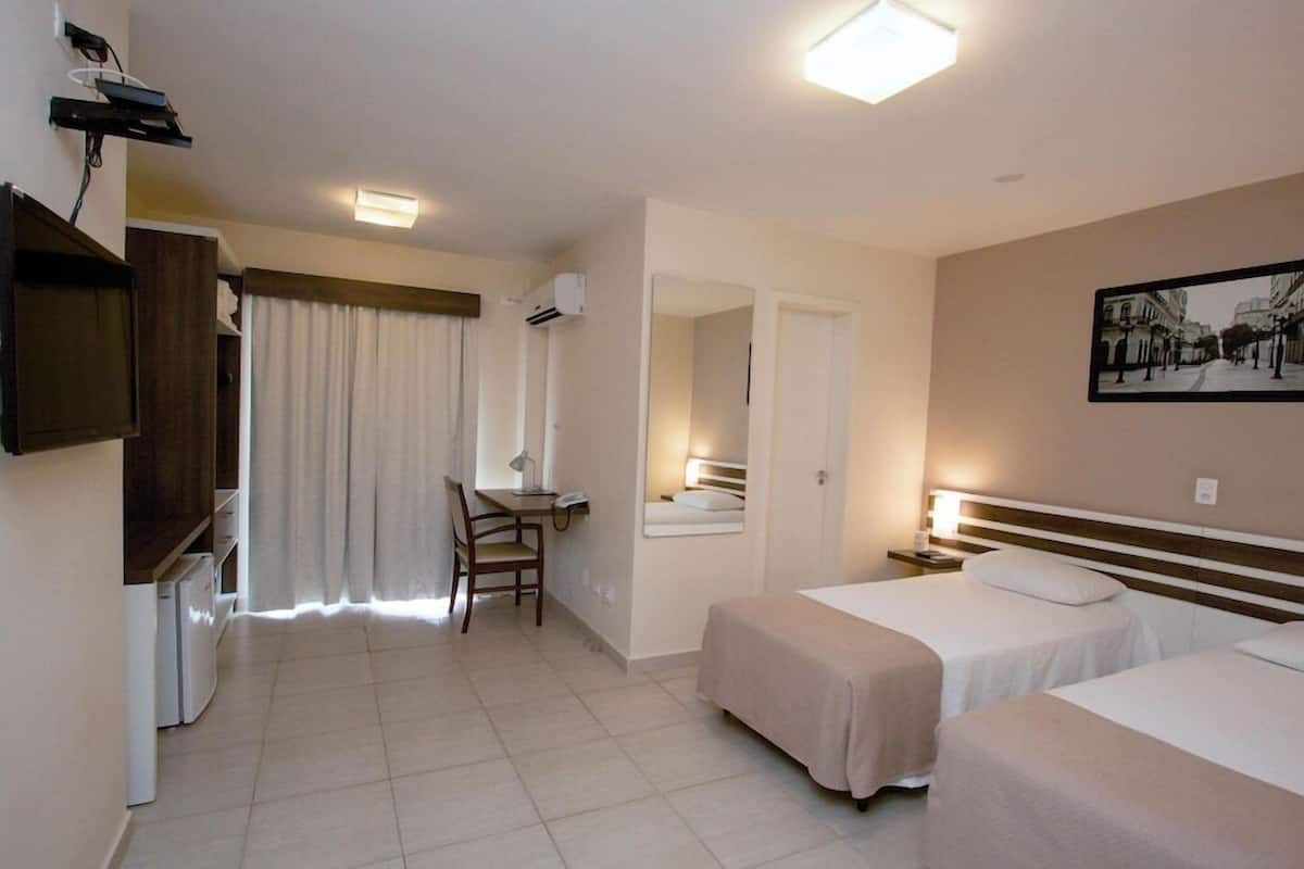 Een hotelkamer met twee bedden, een bureau, een stoel, een televisie en een spiegel.