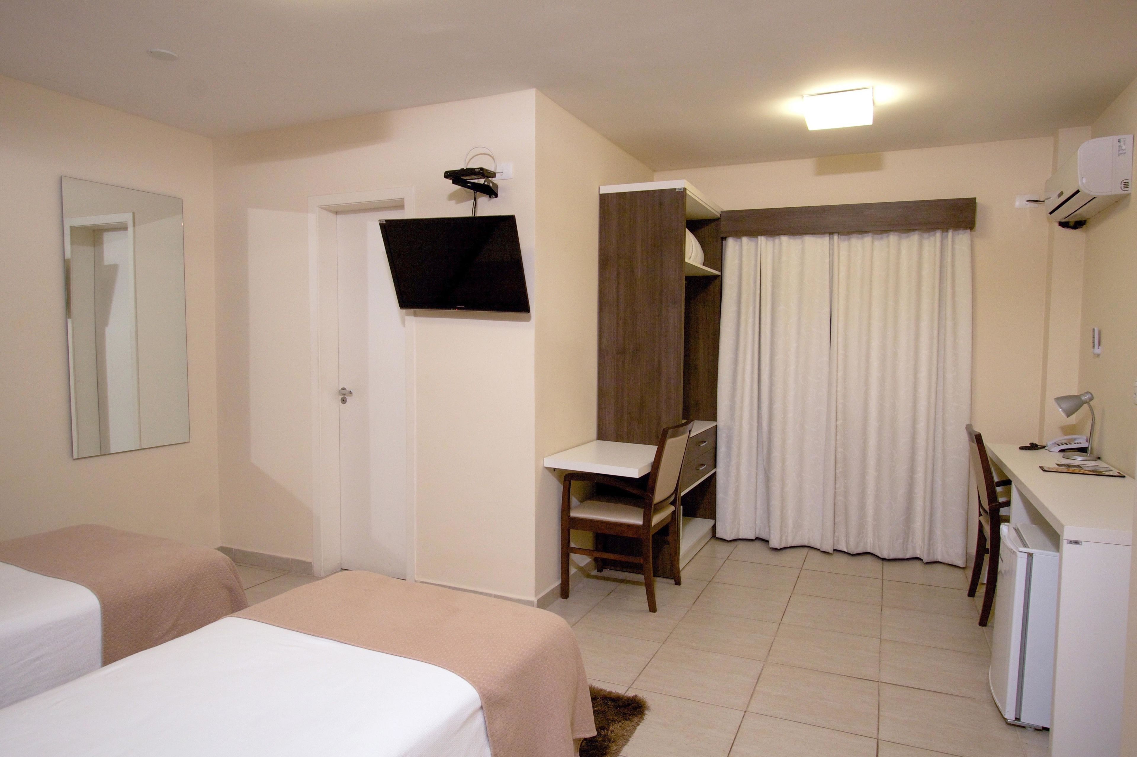 Una habitación de hotel con dos camas, un escritorio con silla, televisor y refrigerador.