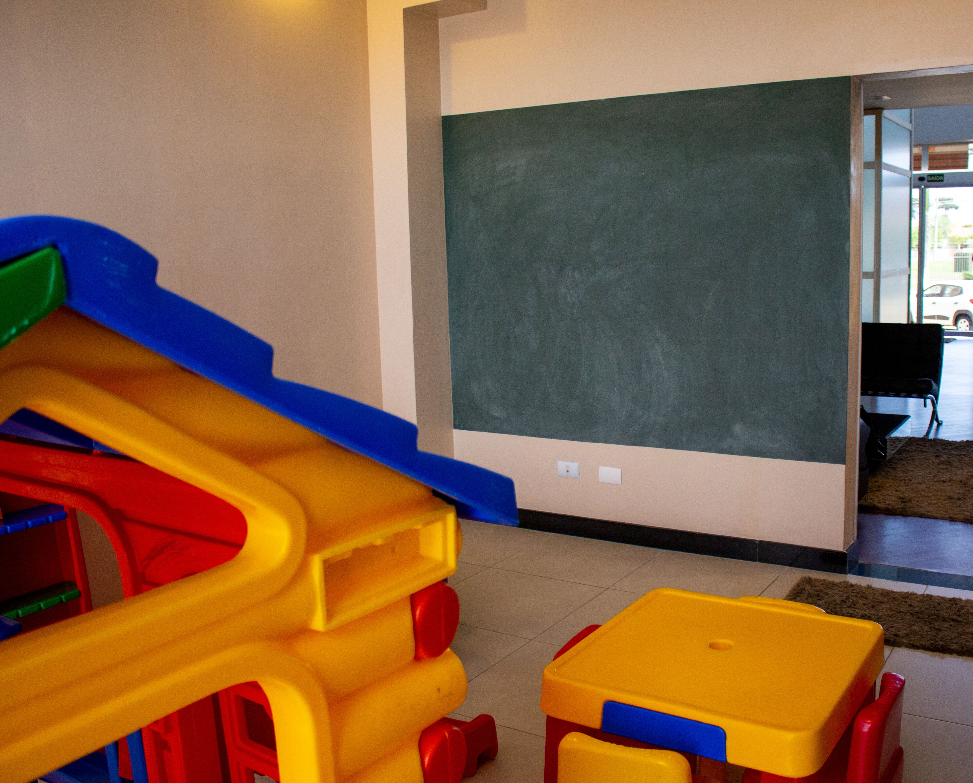 A play area with a slide and a table, a chalkboard, and a door leading outside.
