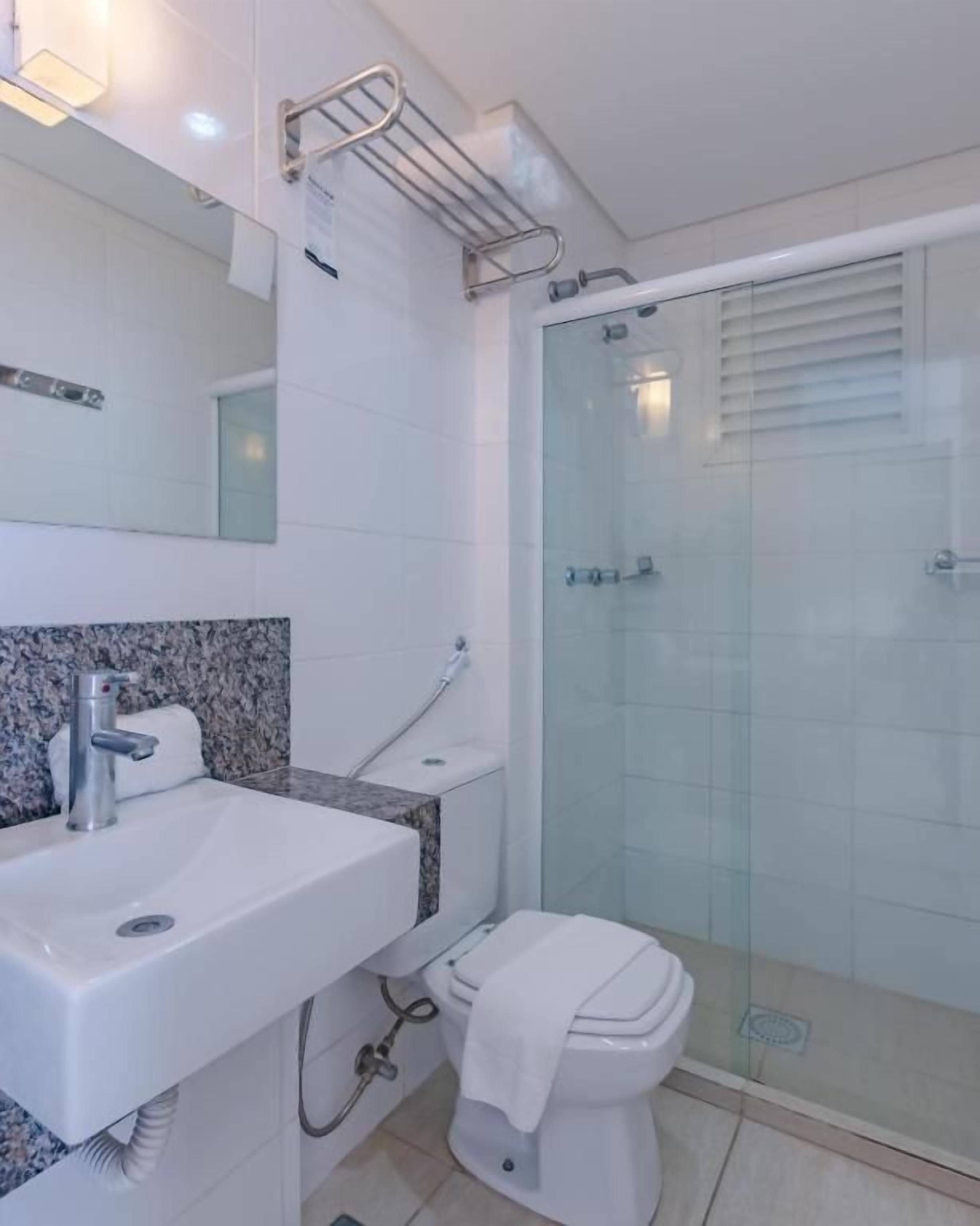 A bathroom with a white sink, a mirror, a glass shower enclosure, and a toilet.