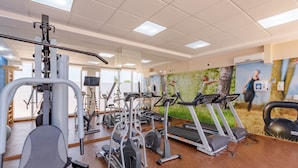 Une salle de sport équipée de divers appareils d’exercice, d’un tapis de course et d’un miroir.